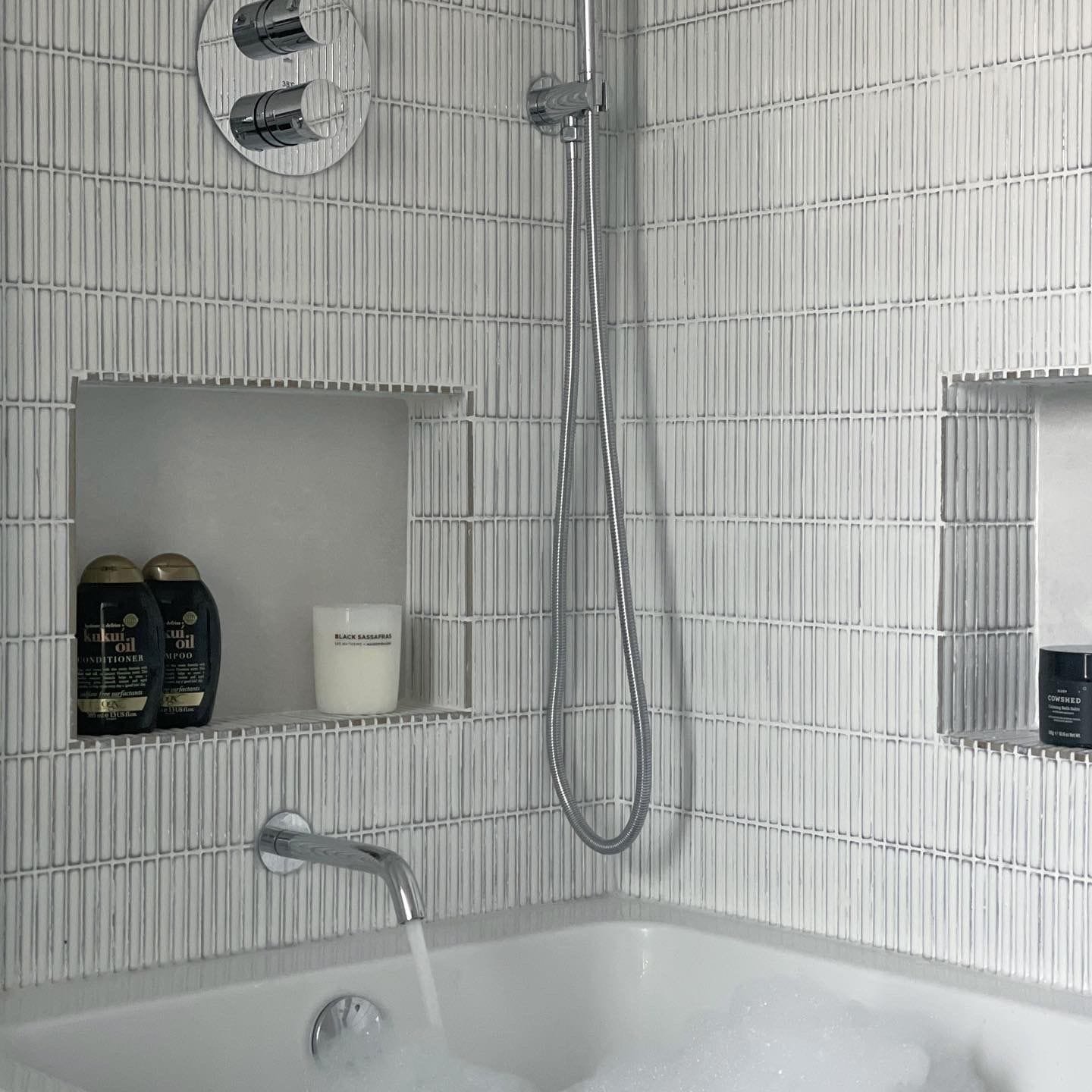 Close-up of a modern bath and shower installation with chrome fittings and recessed storage, expertly plumbed in Weybridge.