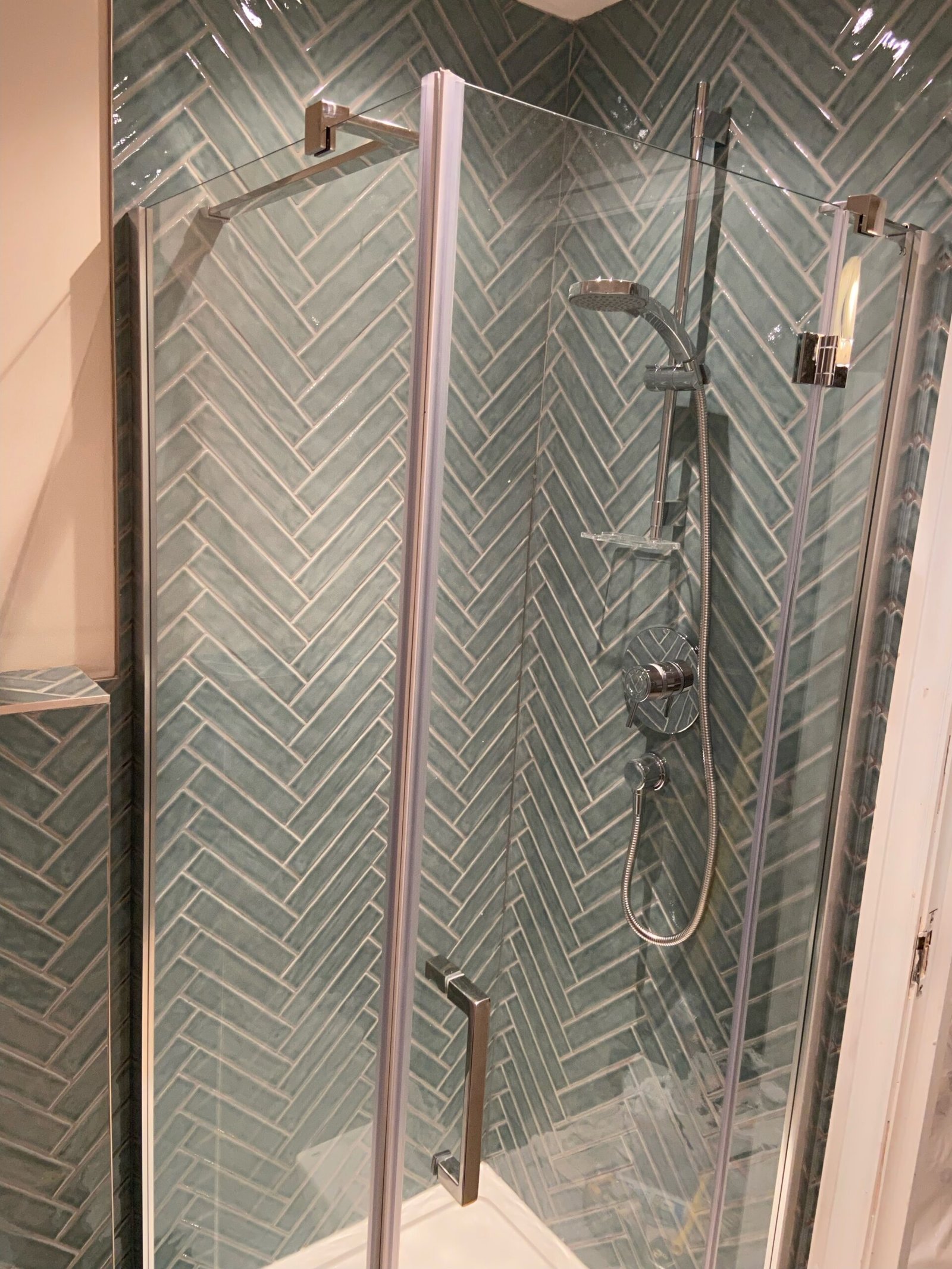Shower enclosure in Weybridge with green herringbone wall tiles and chrome fixtures.