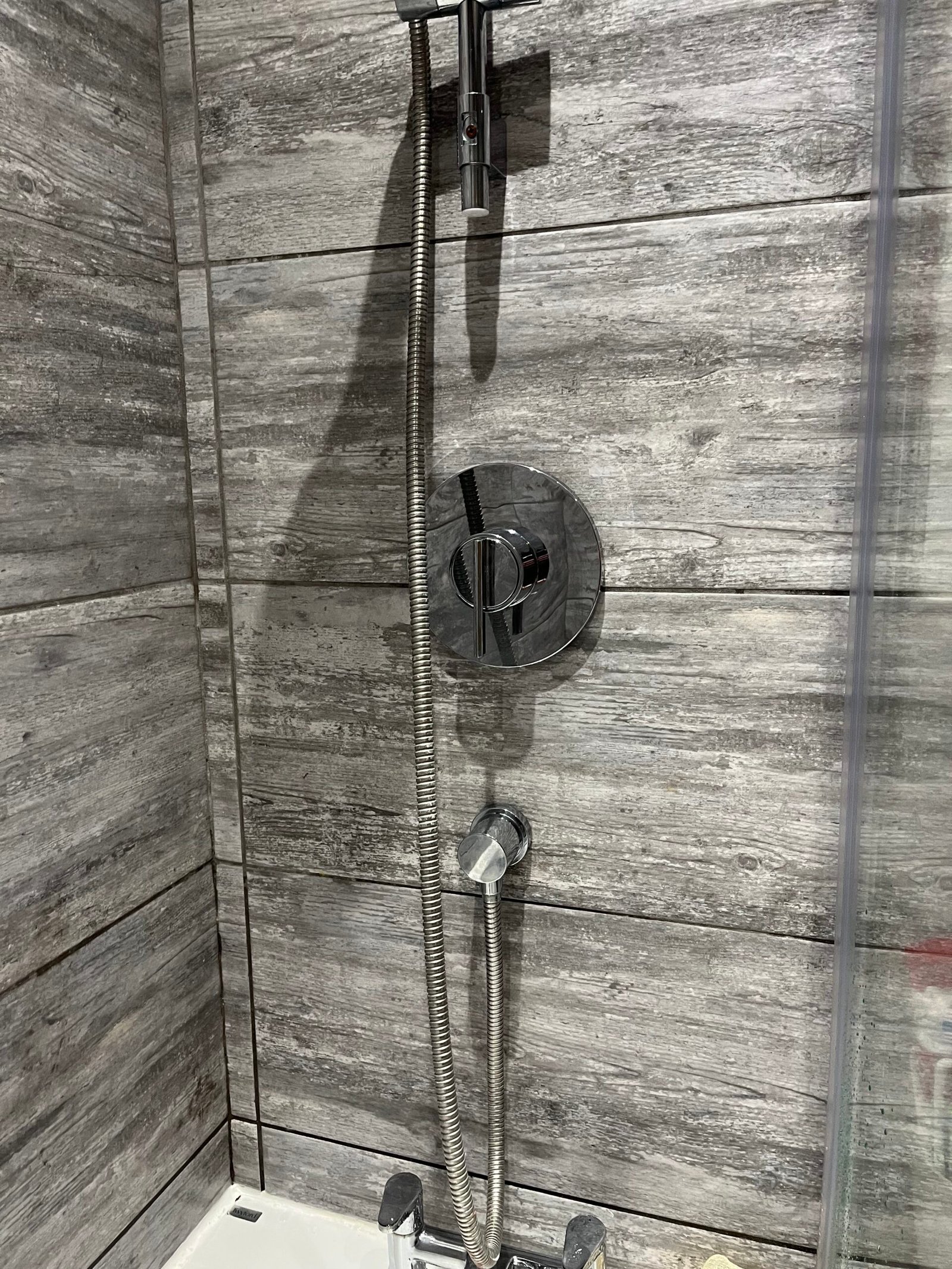 Close-up of a chrome shower valve and mixer tap installed by a plumber in Weybridge with grey stone-effect tiles.