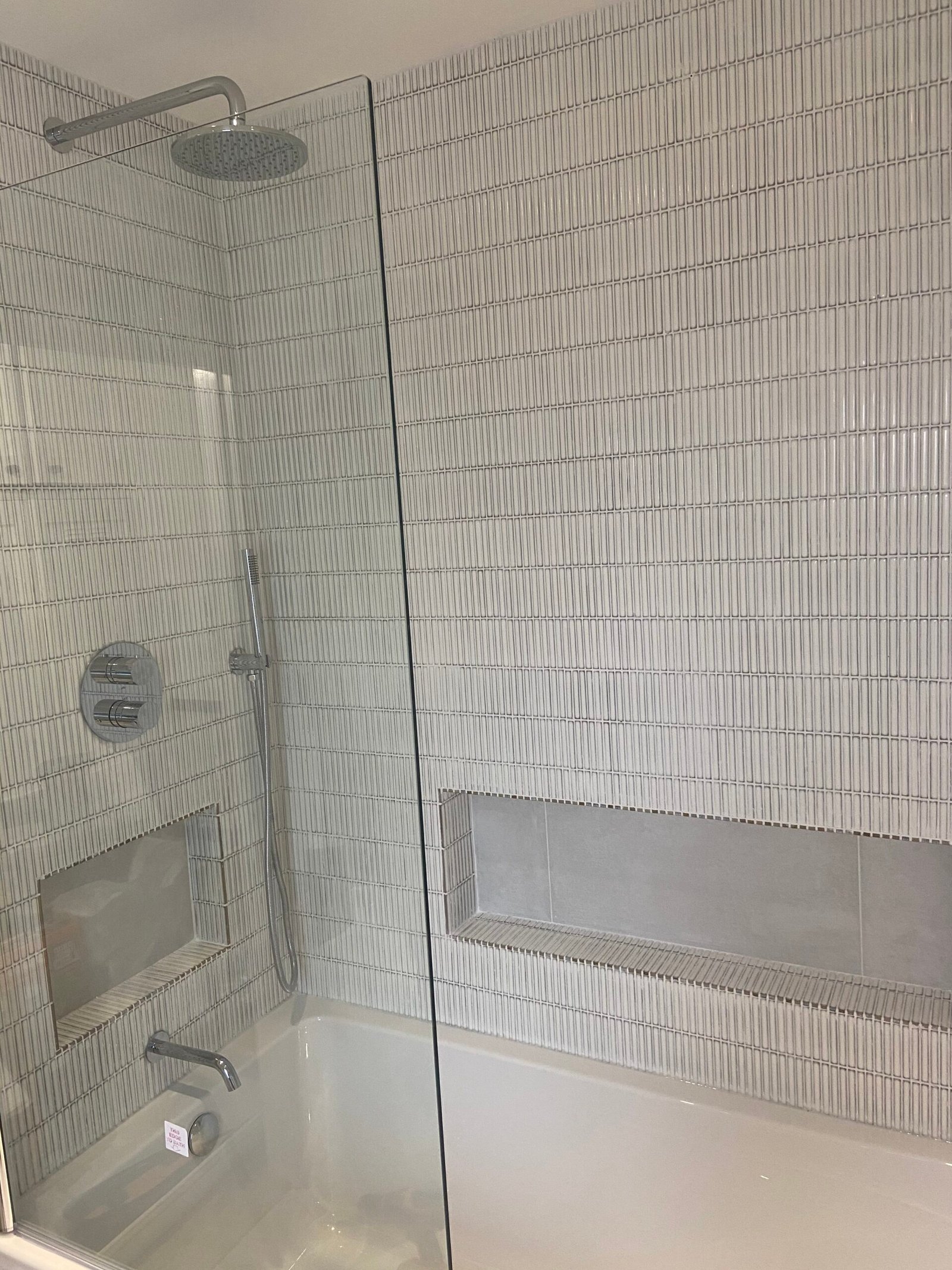 Bathroom tiling in Weybridge with vertical white wall tiles, built-in tiled niches, and a combined bath and shower.